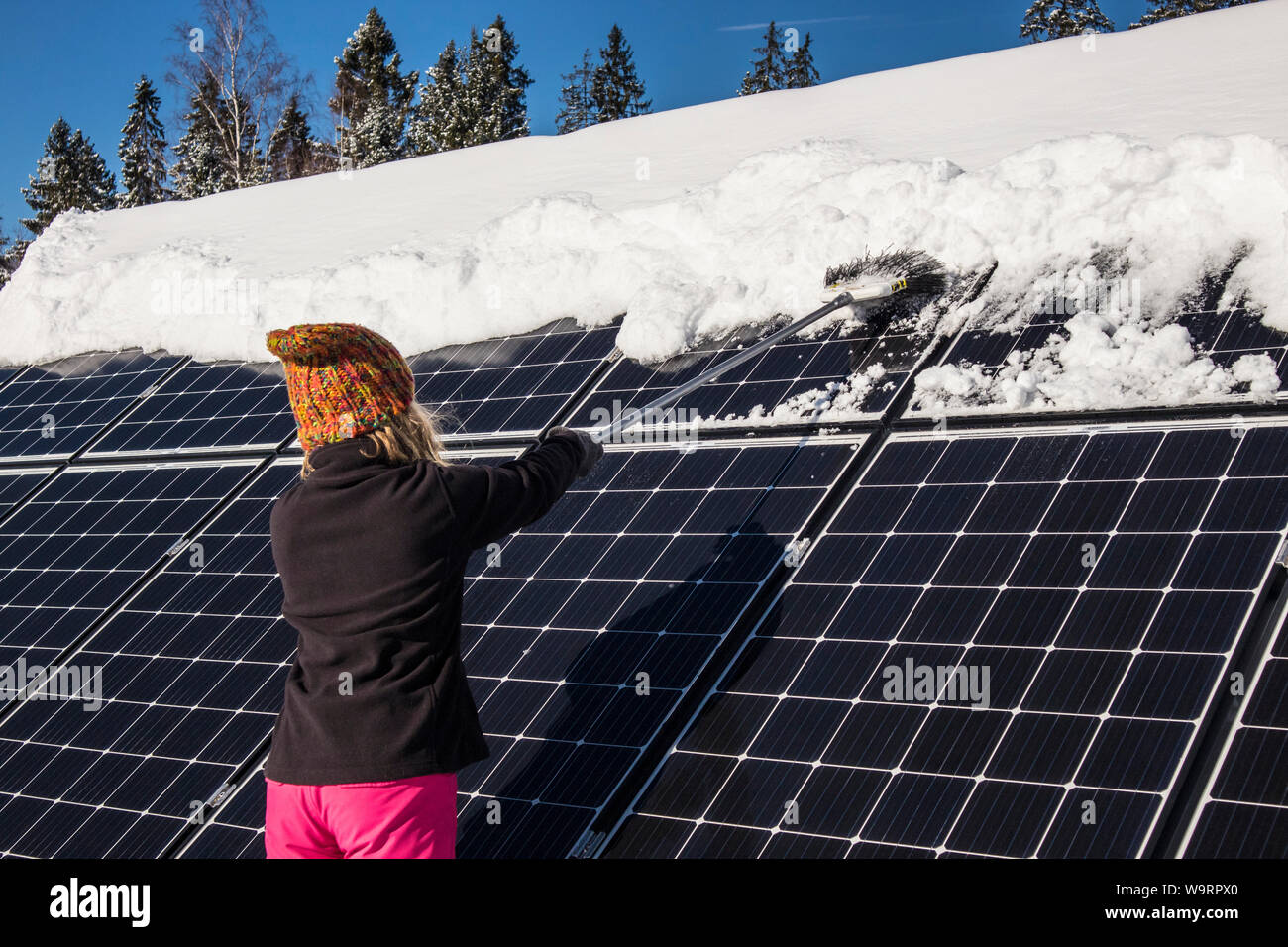 Frau schieben Schnee Solarmodule aus im Winter. Wenn Schnee Panels umfasst, können Sie nicht Strom erzeugen. Die kleinen privaten Home Haus im Hintergrund. Stockfoto