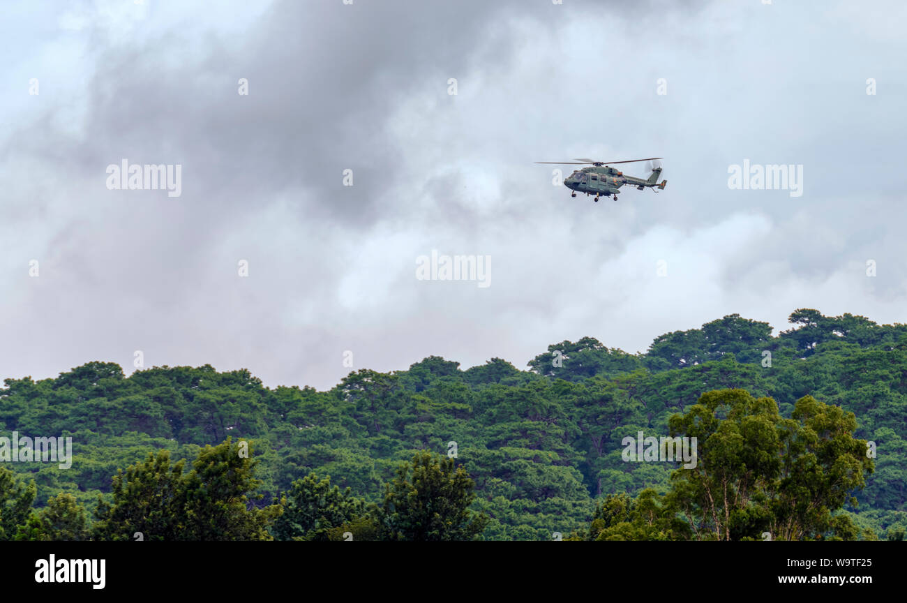 Ein Hubschrauber der indischen Luftwaffe, Dhruv, fliegt über Baumkronen und bereitet sich darauf vor, Blütenblätter bei einer Versammlung zum indischen Unabhängigkeitstag abzuwerfen. Stockfoto