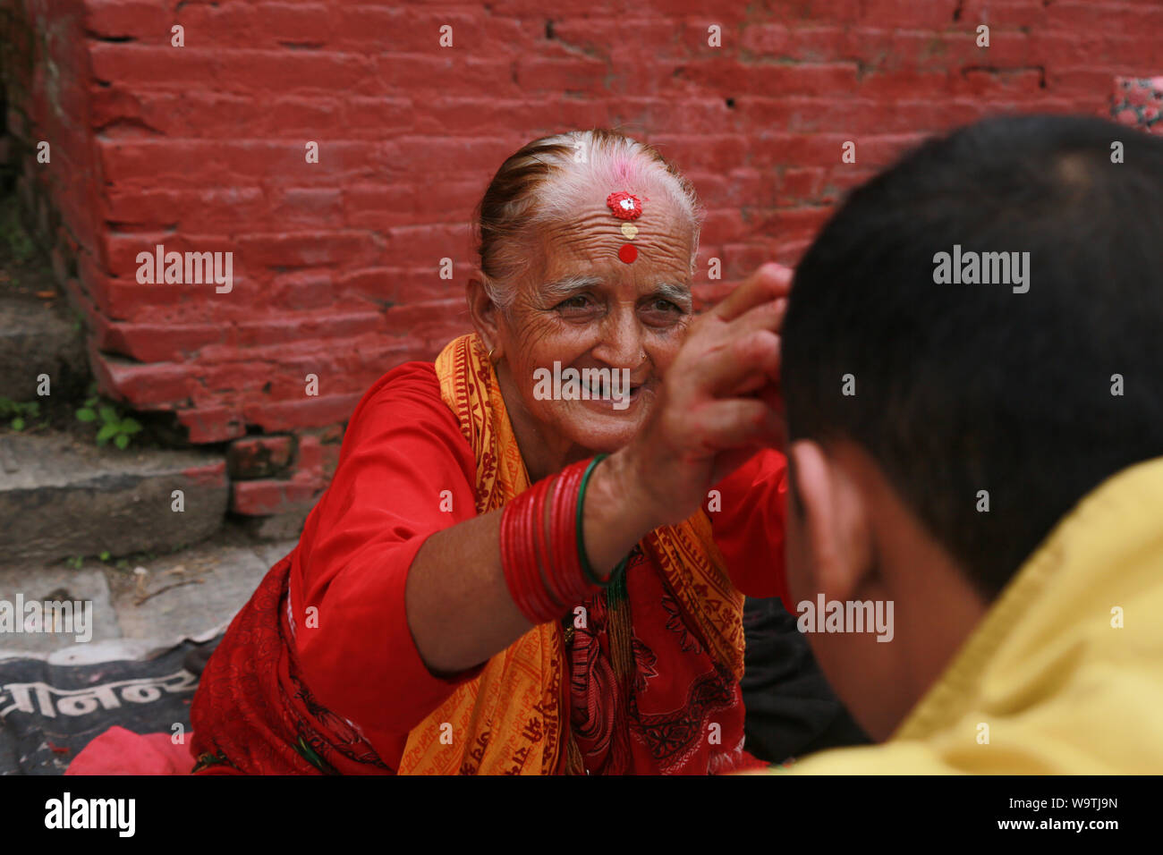 Kathmandu, Nepal. 15 Aug, 2019. Ein Priester Frauen lächeln, wenn Sie eine Tika für Anhänger in Pashupatinath Tempel legen. Sarita Khadka/Alamy leben Nachrichten Stockfoto