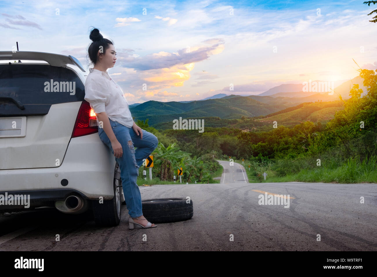 Junge schöne Frau in der Nähe von Auto für den Aufruf um Hilfe auf der öffentlichen Straße im Waldgebiet am Berg und Himmel Hintergrund Stockfoto