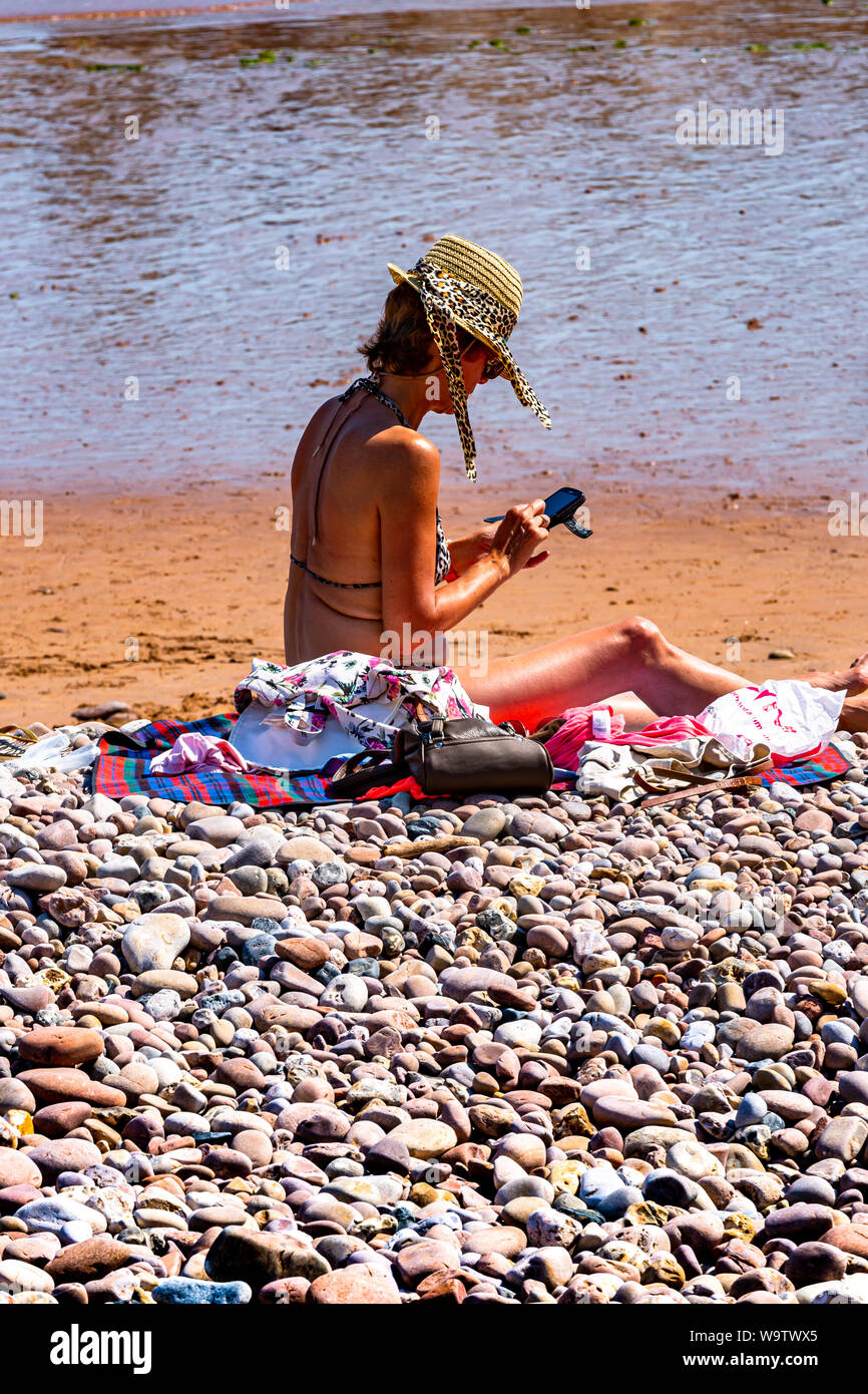 Frau mit Sonnenhut texting, selbst wenn an einem herrlichen Strand in herrlicher Sonnenschein. Stockfoto