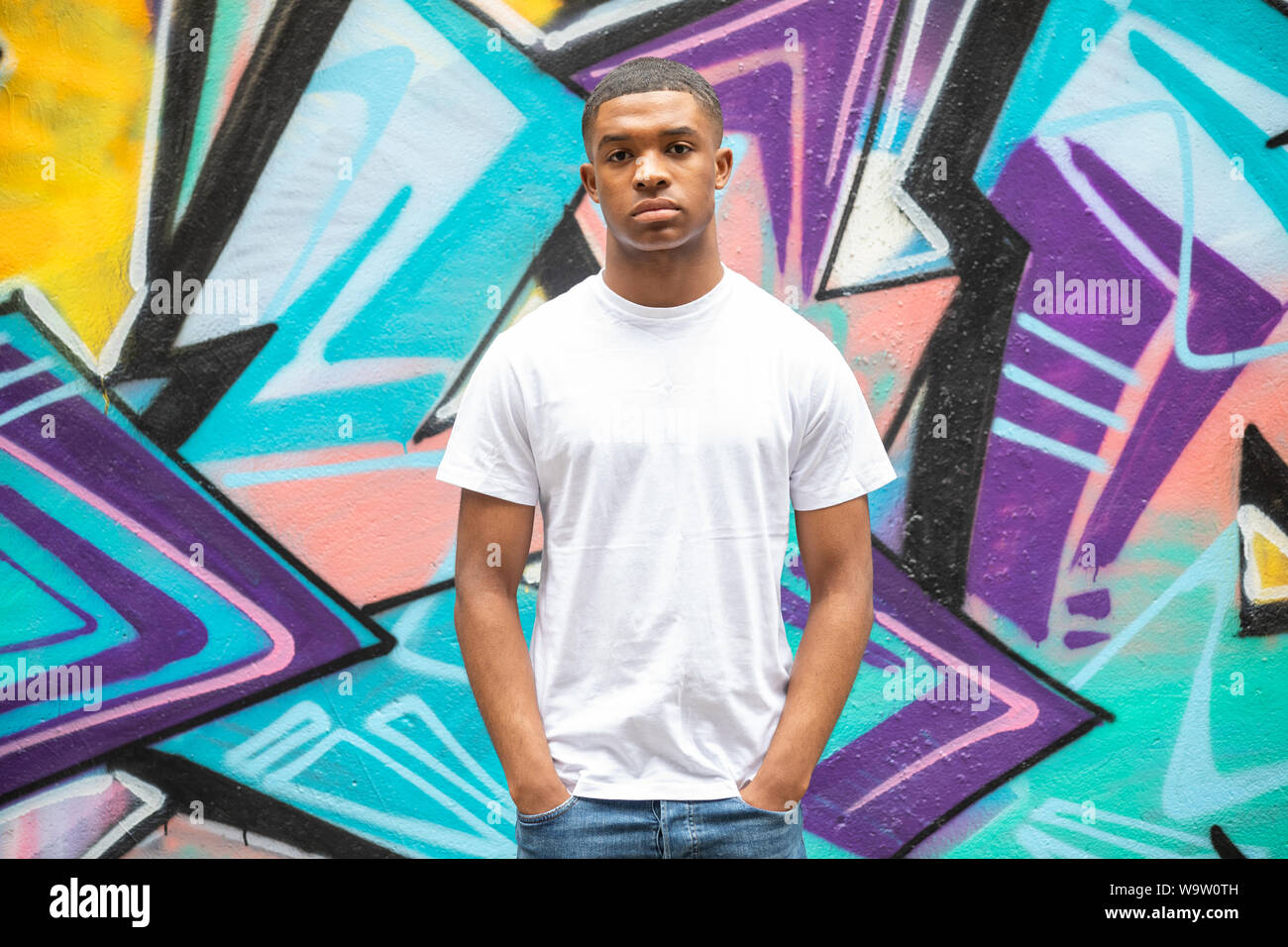 Ein junger Mann stellt sich vor einer grafitti Art Wall auf einer Straße der Stadt in Spitalfields, E1 Stockfoto