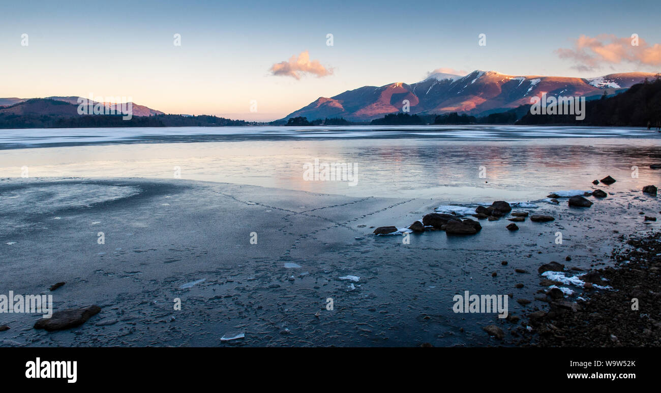 Winter Sonnenaufgang leuchtet der Schnee - dusted Hängen des Skiddaw Berg über einen gefrorenen Derwent Water in England Lake District. Stockfoto