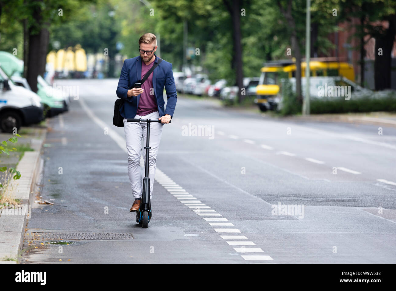 Ein junger Geschäftsmann mit Mobiltelefon, einen Elektroroller auf der Straße Stockfoto