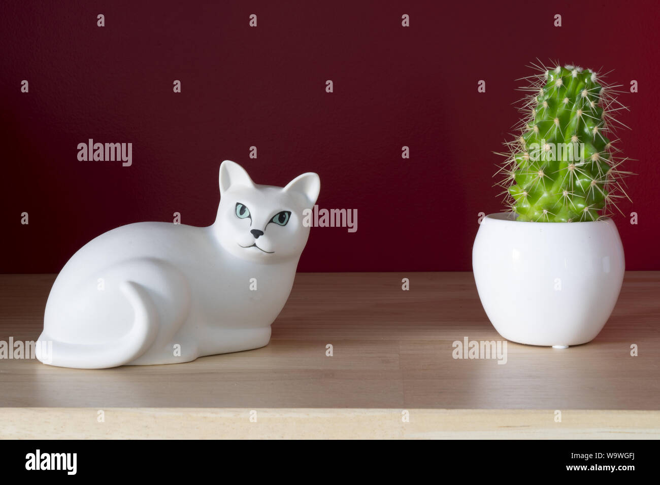 Ein weißer Keramik Katze und kleinen Kaktus auf einem Regal mit einer roten Wand Stockfoto