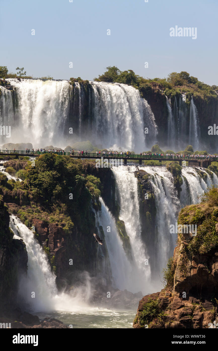 Steg voller Touristen in der Nähe der Wasserfälle von Iguazu Fluß in sonnigen Sommertag. Foz de Iguaçu teilt die Grenze zwischen Brasilien und Argentinien und ist Stockfoto