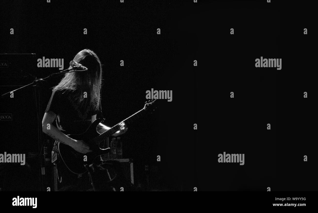 Männlicher Musiker spielt Gitarre auf einer Bühne in der Nähe des Mikrofons In schwarz und weiß Stockfoto