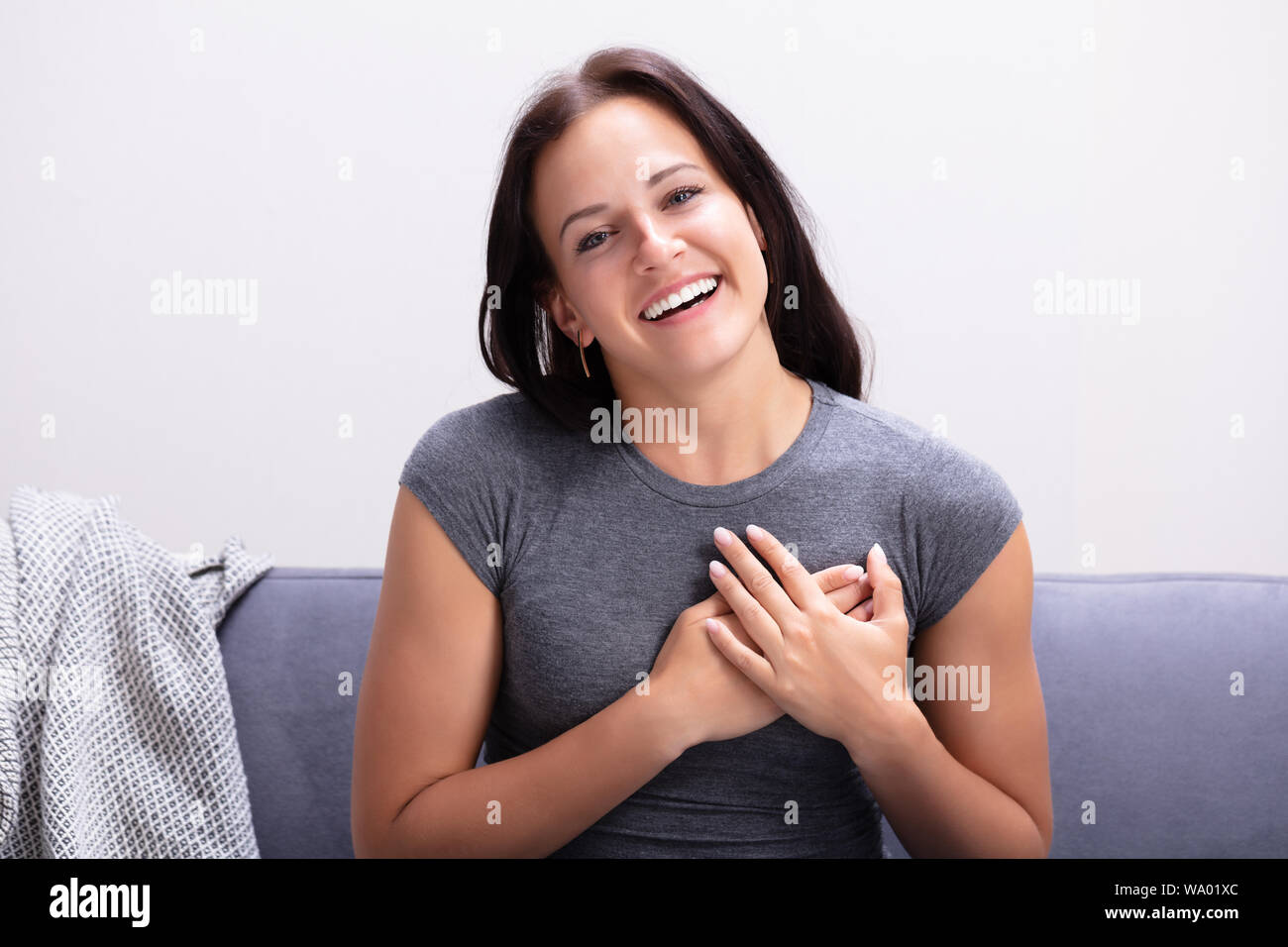 Glückliche junge Frau sitzt auf einem Sofa ihre Hand auf Herz halten Stockfoto