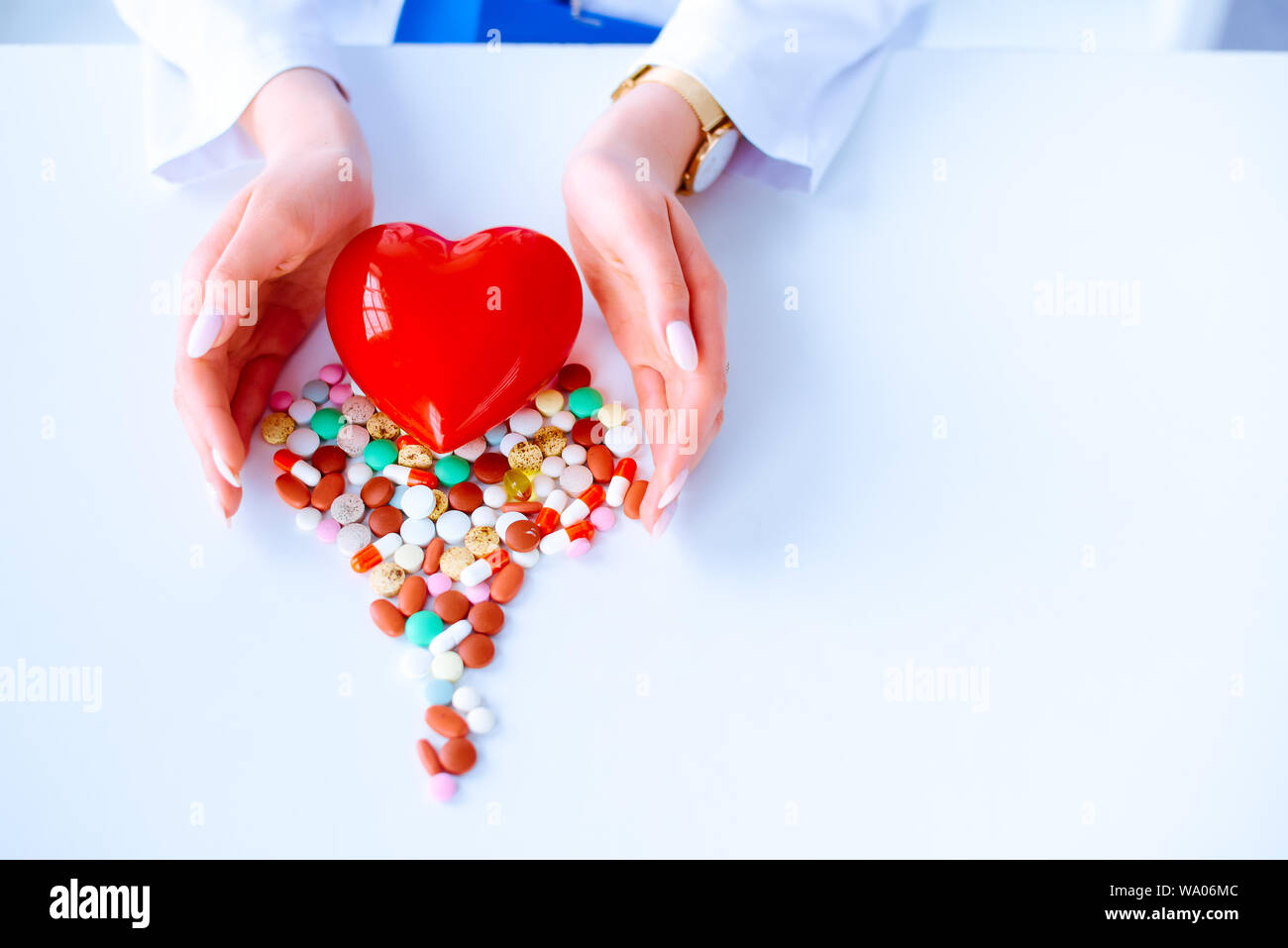 Bunte Pillen auf einem Tisch in der Form eines Herzens auf einem weißen Hintergrund. Rotes Herz. Doctor's Hände auf den Tisch in der Nähe des Herzen und Pillen. Konzept Stockfoto