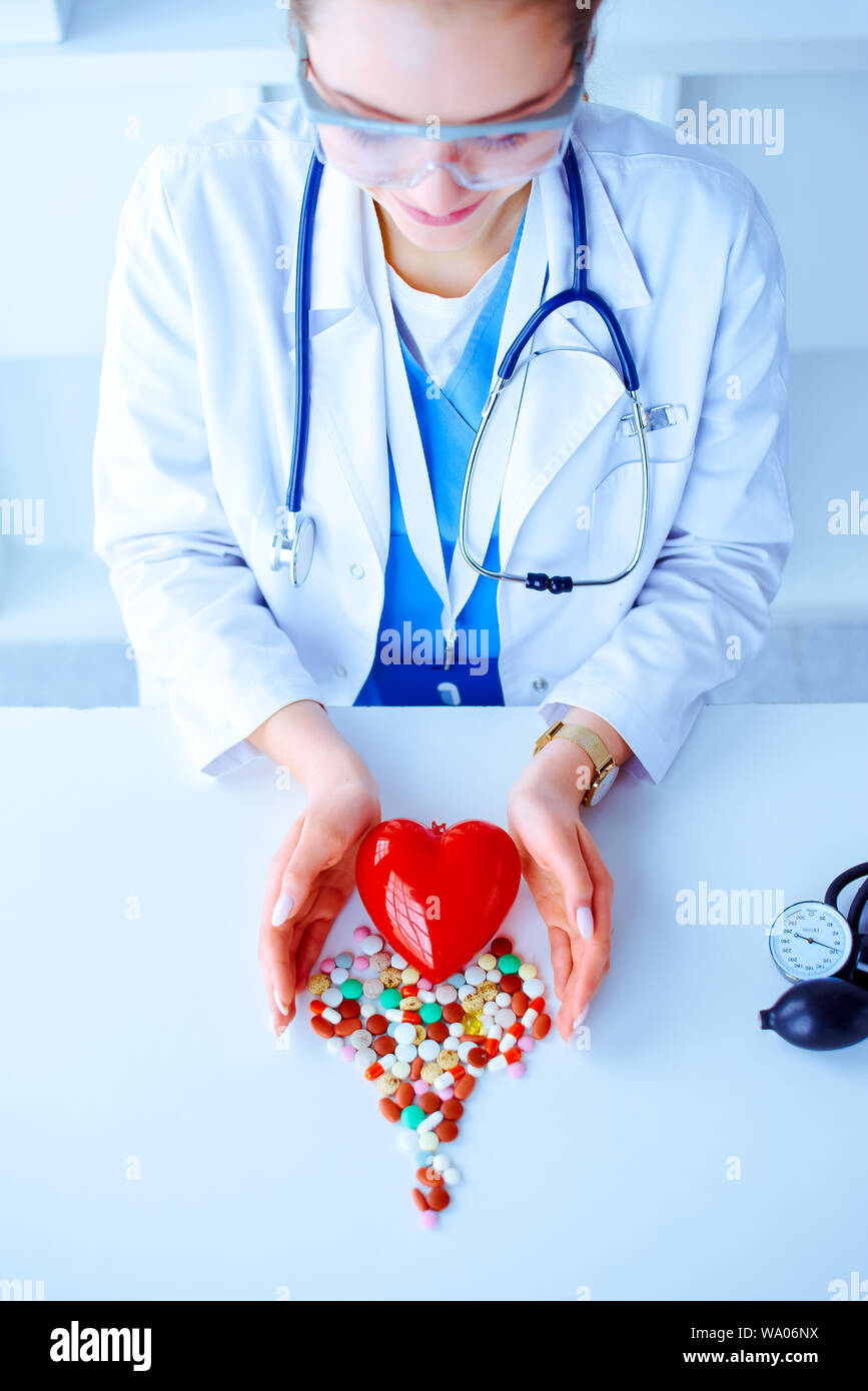 Bunte Pillen auf einem Tisch in der Form eines Herzens auf weißem Hintergrund und tonometer. Rotes Herz. Doctor's Hände auf den Tisch in der Nähe des Herzen und Pille Stockfoto