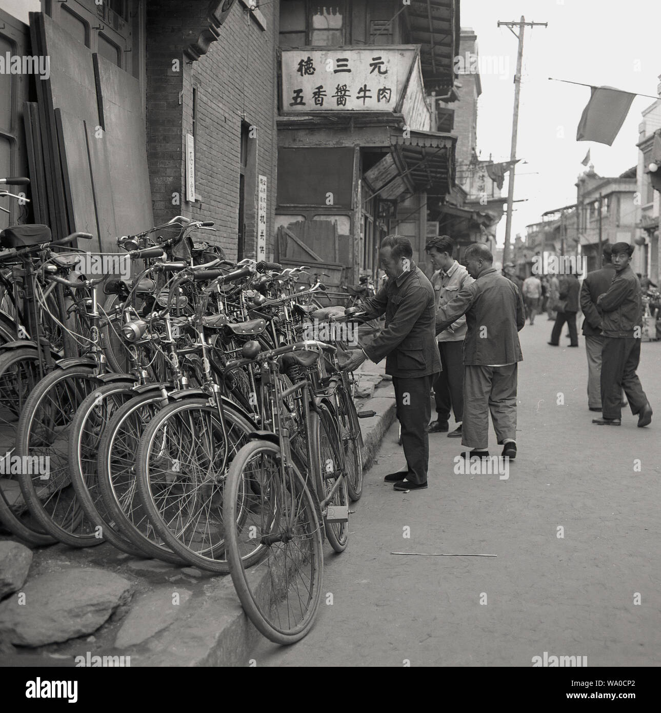 1950 s, historischen, lokalen chinesischen Männer mit ihren Fahrrädern Nebeneinander außerhalb eines Gebäudes in einer Straße in Peking, China, gestapelt. Bekannt als das Königreich von Fahrrädern" - von der Kommunistischen Partei gefördert als kostengünstige Lösung für die öffentlichen Verkehrsmittel - es in dieser Ära war, dass Fahrrad wurde das wichtigste Transportmittel für die meisten städtischen Chinesisch, vorlagentyps, der die Fahrradrikscha (Cycle rickshaw) der 1940er Jahre und die Hand gezogenen Rikscha der 1920er und 30er Jahre. Stockfoto