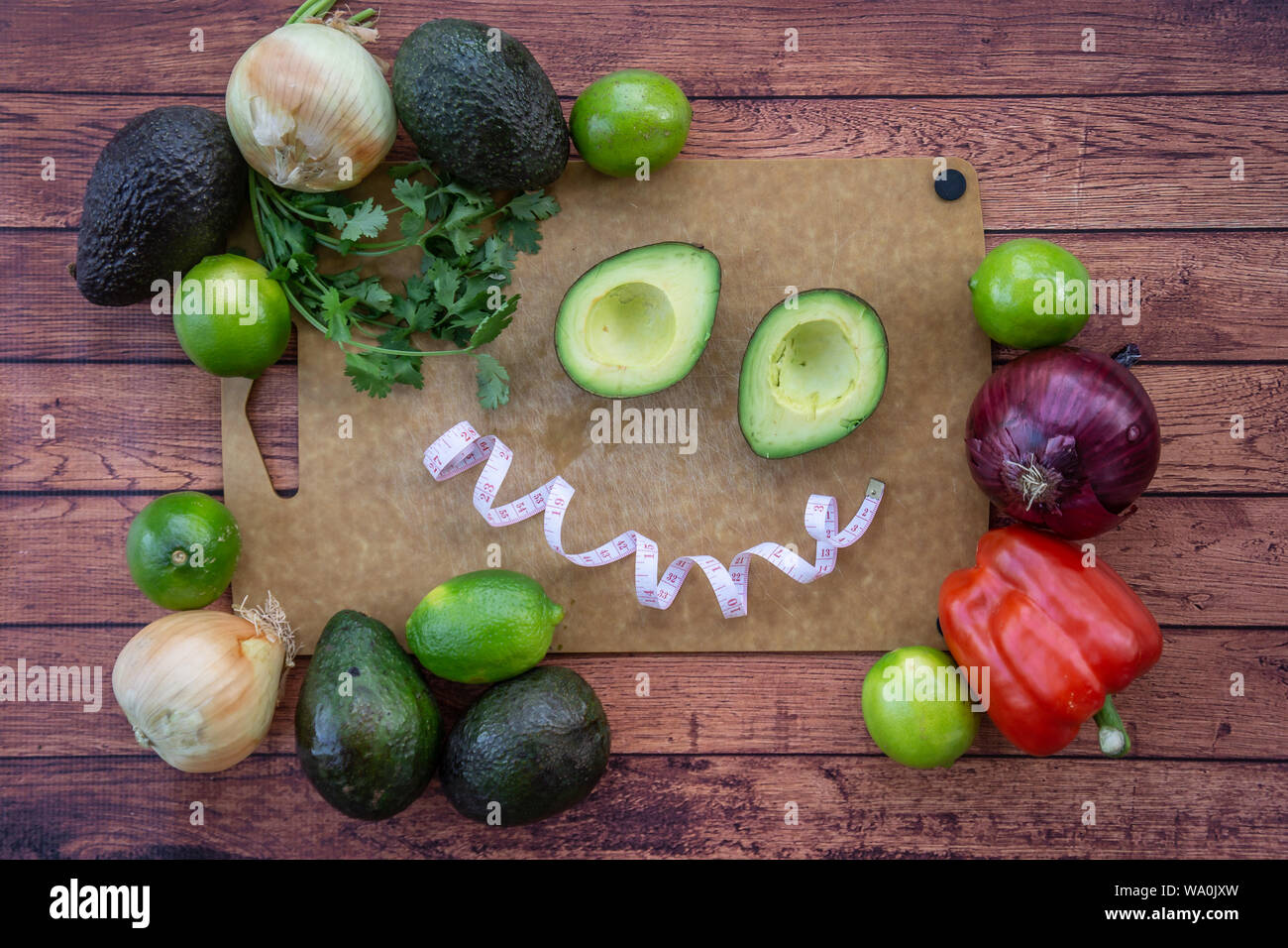 Glücklich lächelnde Gesicht mit halbierte Avocado, frischer Koriander, und guacamole Zutaten. Blick von oben auf die Lebensmittel mit einem Lächeln. Gesund abnehmen mit natürlichen Nahrungsmitteln o Stockfoto