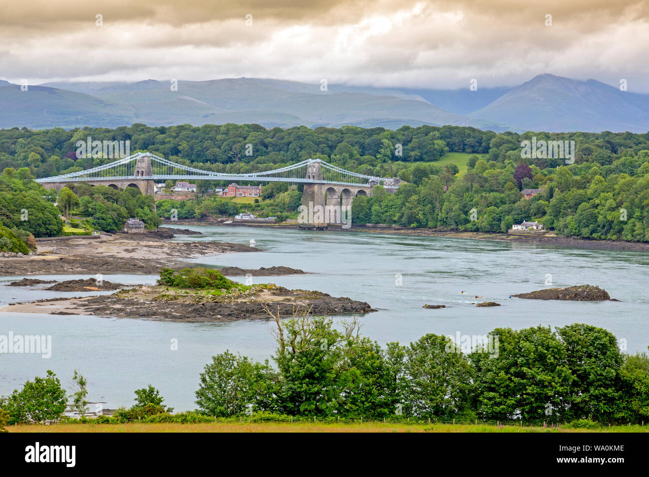 Die historische 1826 Menai Bridge von Thomas Telford nimmt die 5 Straße über die Menai Straits in Anglesey, mit den Bergen von Snowdonia jenseits, Wales, Großbritannien Stockfoto