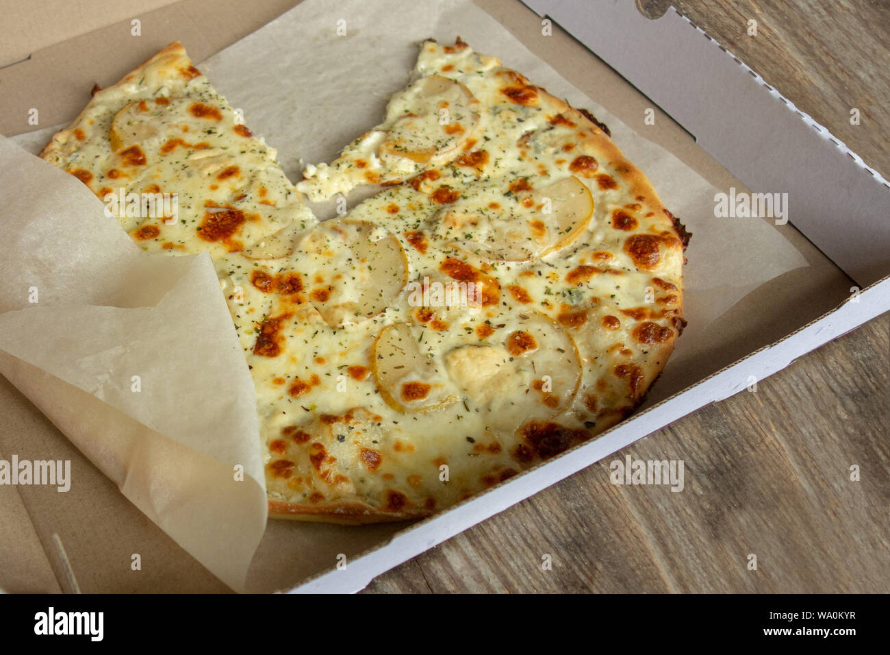 Käse Pizza mit Birnen im Karton Aufenthalt auf Holztisch. Close up Perspektive betrachten. Eine Scheibe oder ein Stück fehlt. Mahlzeit ist auf weißem Küche papier Stockfoto
