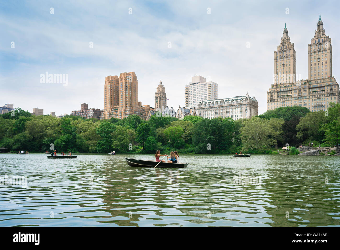 New York Central Park, Ansicht im Sommer von Menschen Ruderboote auf dem See mit West Central Park Gebäude im Hintergrund, Manhattan, NYC, USA Stockfoto