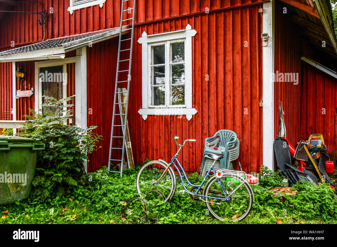 Rückstände und Elemente außerhalb einer rustikalen Red Ranch Haus mit einem Fahrrad, gestapelte Stühle und eine Leiter im Dorf Porvoo, Finnland links Stockfoto