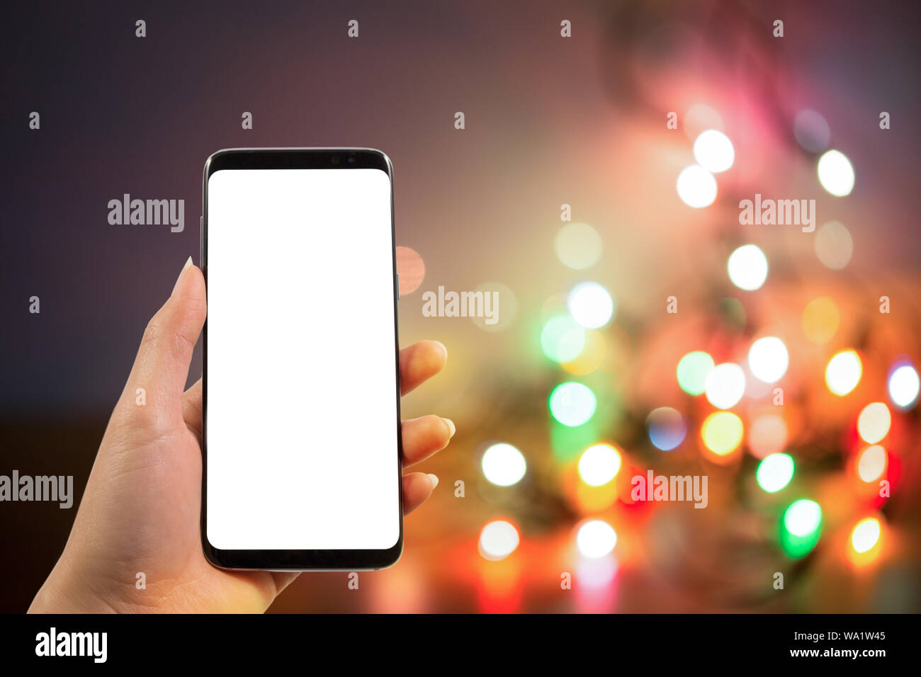 Hand Smartphone mit unscharfen Weihnachtsbeleuchtung Hintergrund mit Kopie Raum warm Retro Vintage Ton. Stockfoto