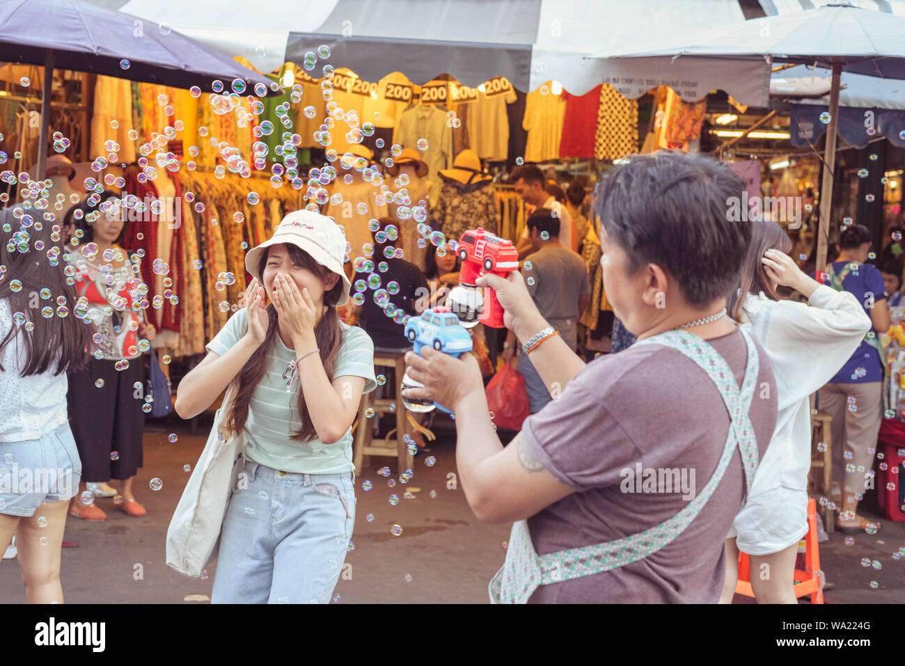 Bangkok, Thailand: Die junge Frau lacht ihr Gesicht verstecken mit Händen in Wolke von Seifenblasen der Verkäufer bubble Gebläse an der berühmten Chatuchak Markt geschickt Stockfoto