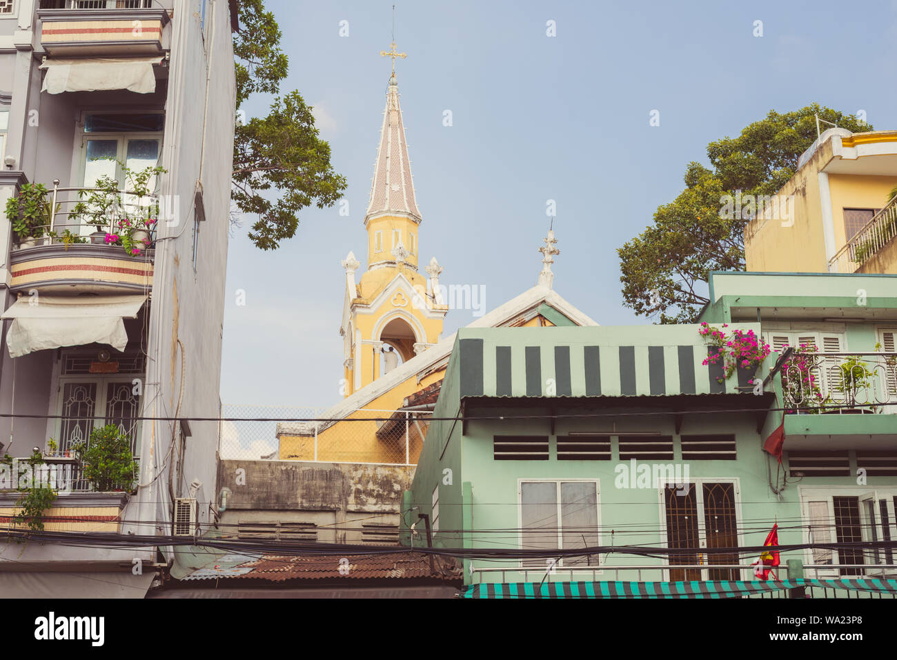 Malerische Balkone von Wohnhäusern mit blühenden Topfpflanzen & Cha Tam Kirche (St. Franz Xaver Pfarrei) Cho Lon-Ho Chi Minh City, Vietnam. Stockfoto