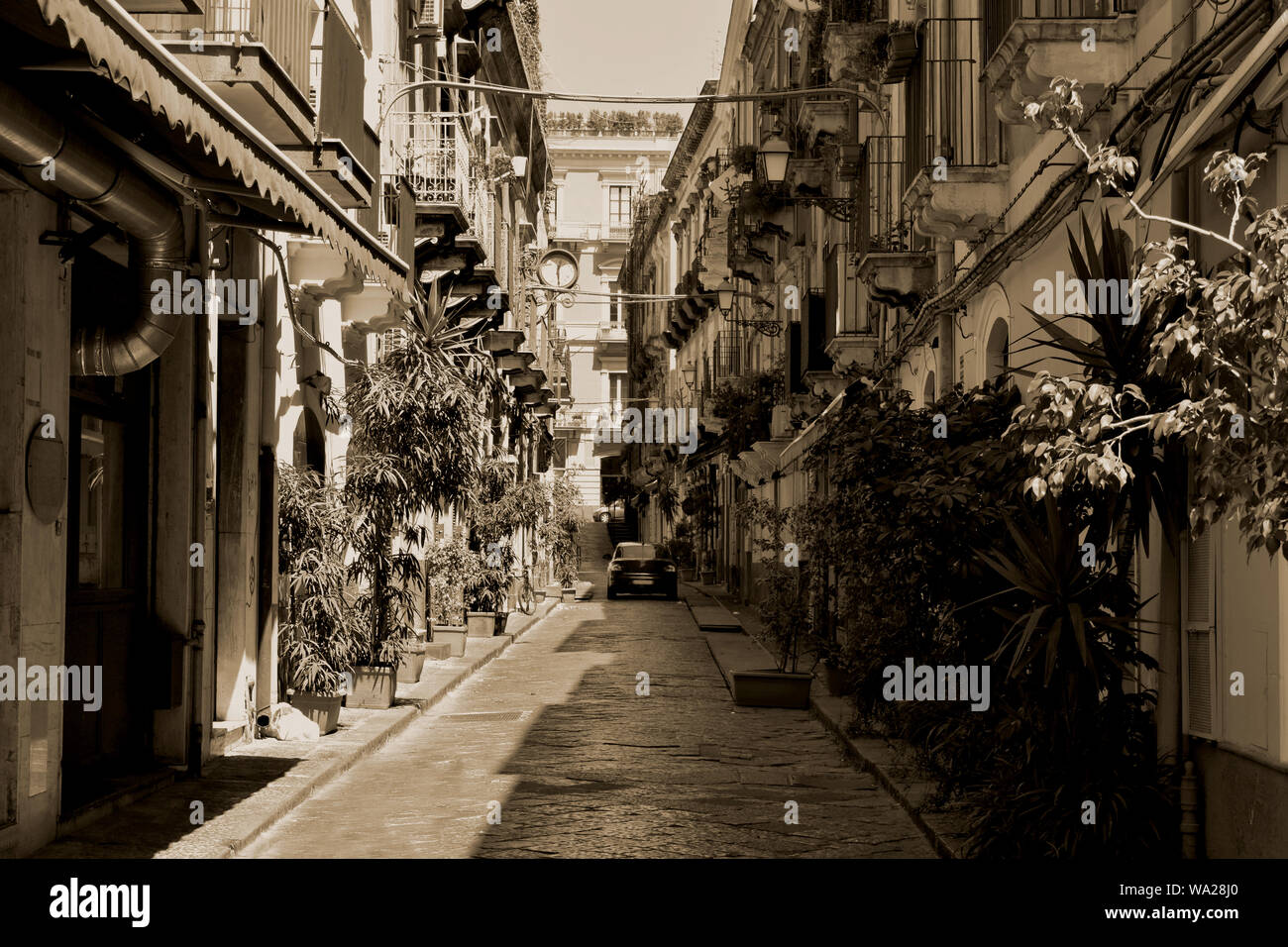 Typische italienische Straße in Catania. Gepflasterte Straße mit wenig Bäume und Häuser mit kleinen Balkonen auf beiden Seiten. Schwarz und Weiß Stockfoto