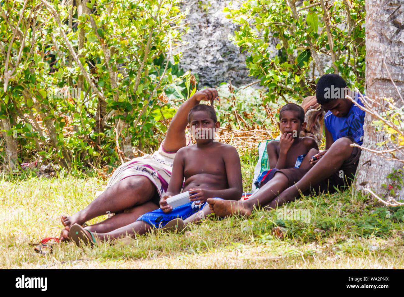 Lifou, Neukaledonien - 9. Januar 2014: Kinder Entspannen unter den Schatten eines Baumes. Das Leben ist sehr zurück in den Südpazifik. Stockfoto