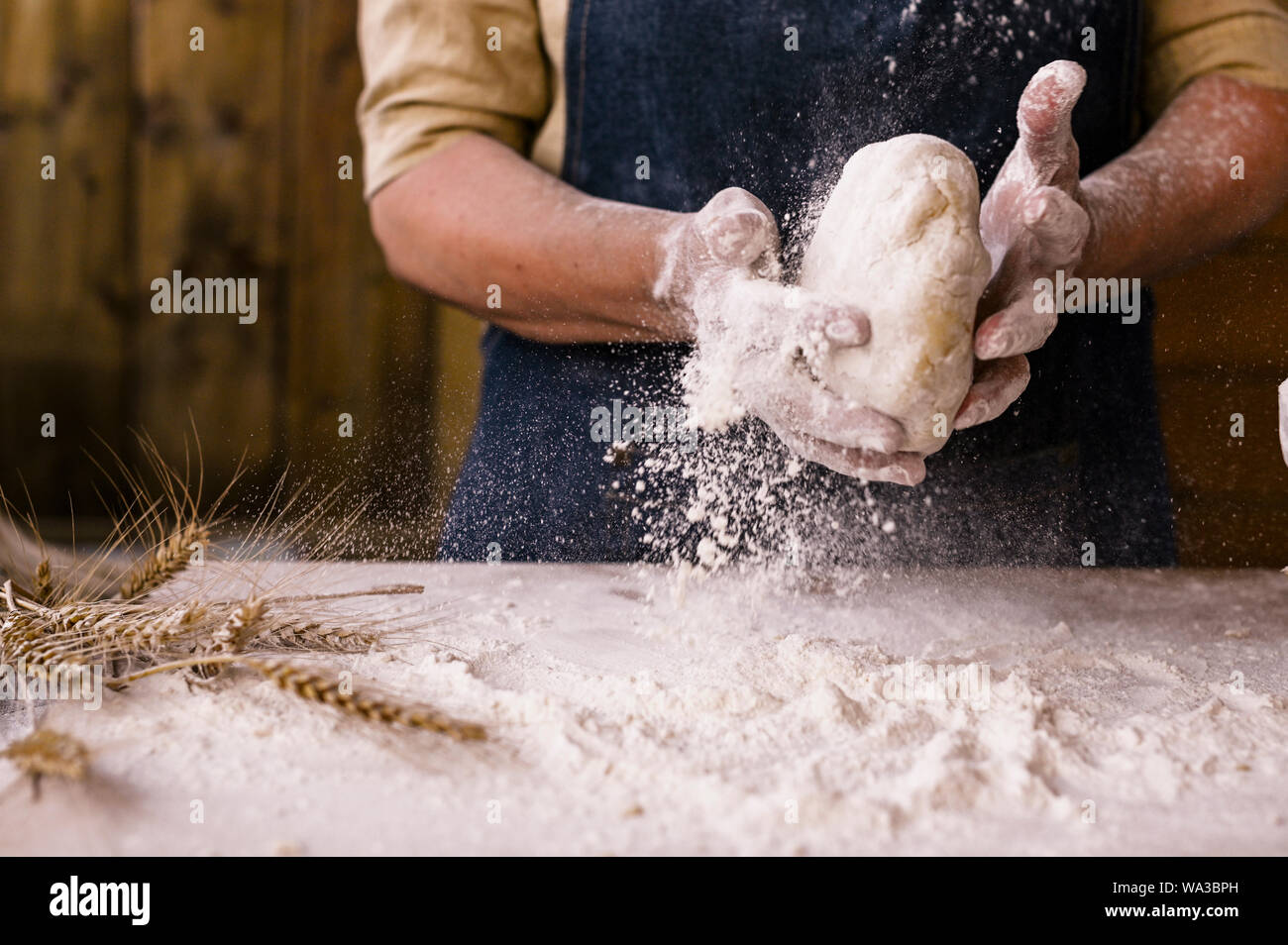 Frauenhand, Mehl und Teig. Levitation in einem Rahmen aus Teig und Mehl. Eine Frau in einer Schürze bereitet Teig für das Backen zu Hause vor. Foto im rustikalen Stil Stockfoto