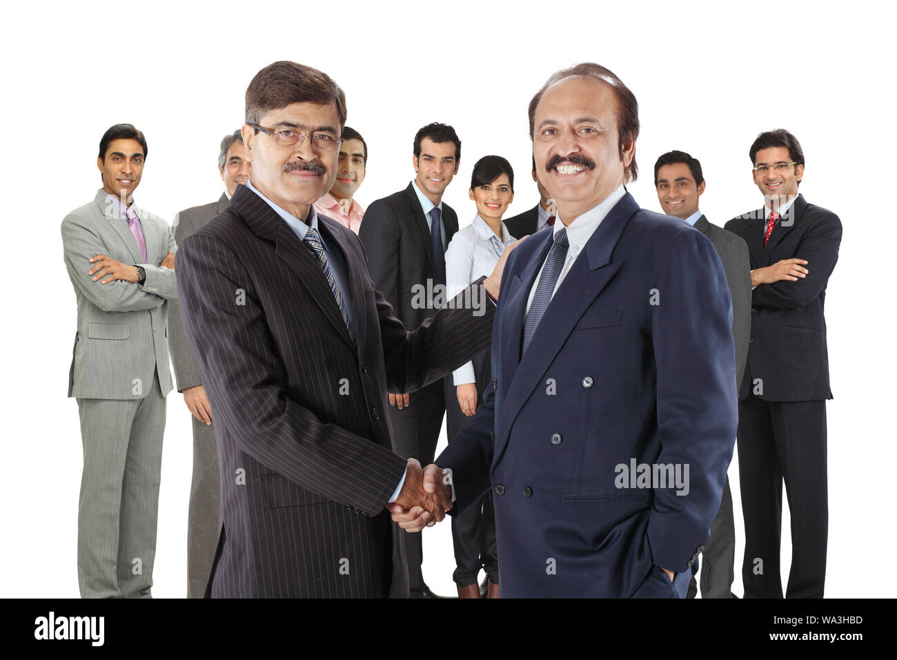 Zwei Führungskräfte schütteln sich die Hände mit ihren Kollegen im Hintergrund Stockfoto
