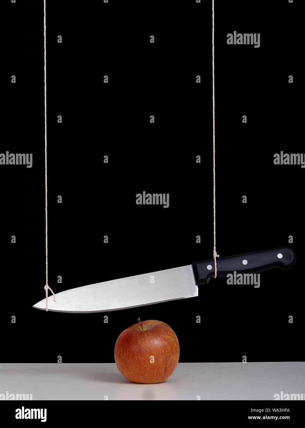 Damoklesschwert Bedrohung, Gefahr, Konzept, Metapher - großes Messer gebunden und über Apple ausgesetzt. Stillleben mit schwarzem Hintergrund. Stockfoto