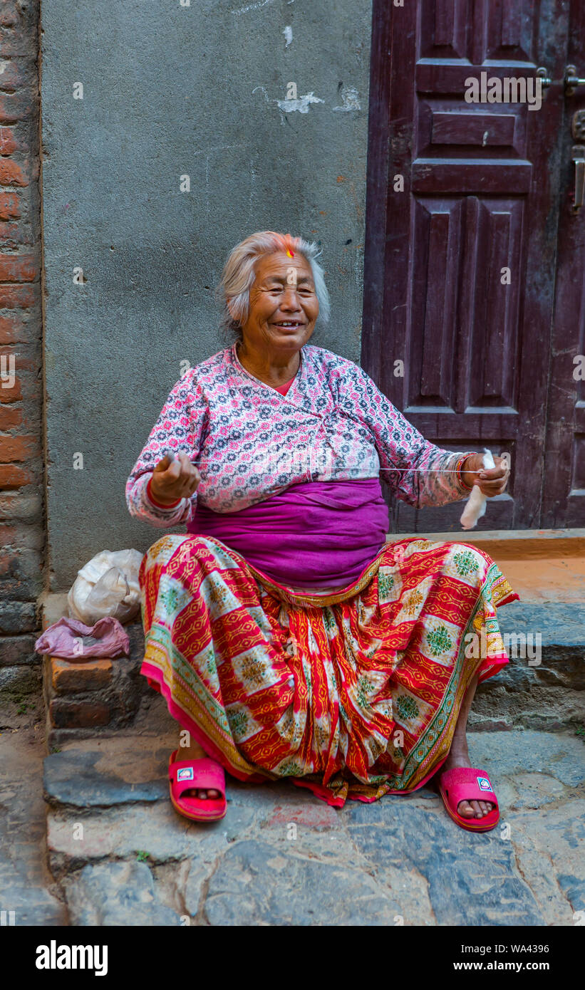 Lächelnd asiatischen älterer Frauen sitzt auf einem Bürgersteig und ist Spinnen von Wolle Stockfoto