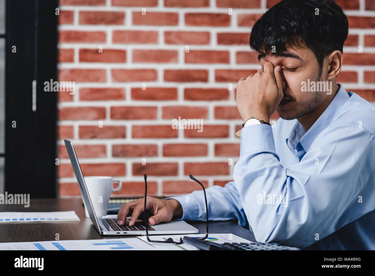 Asiatische Geschäftsmann Stress und Kopfschmerzen beim Arbeiten mit Laptop auf dem Schreibtisch bei der moderne Büro. Business fail Konzept. Mann gefangen Auge wenn überarbeitet. Stockfoto