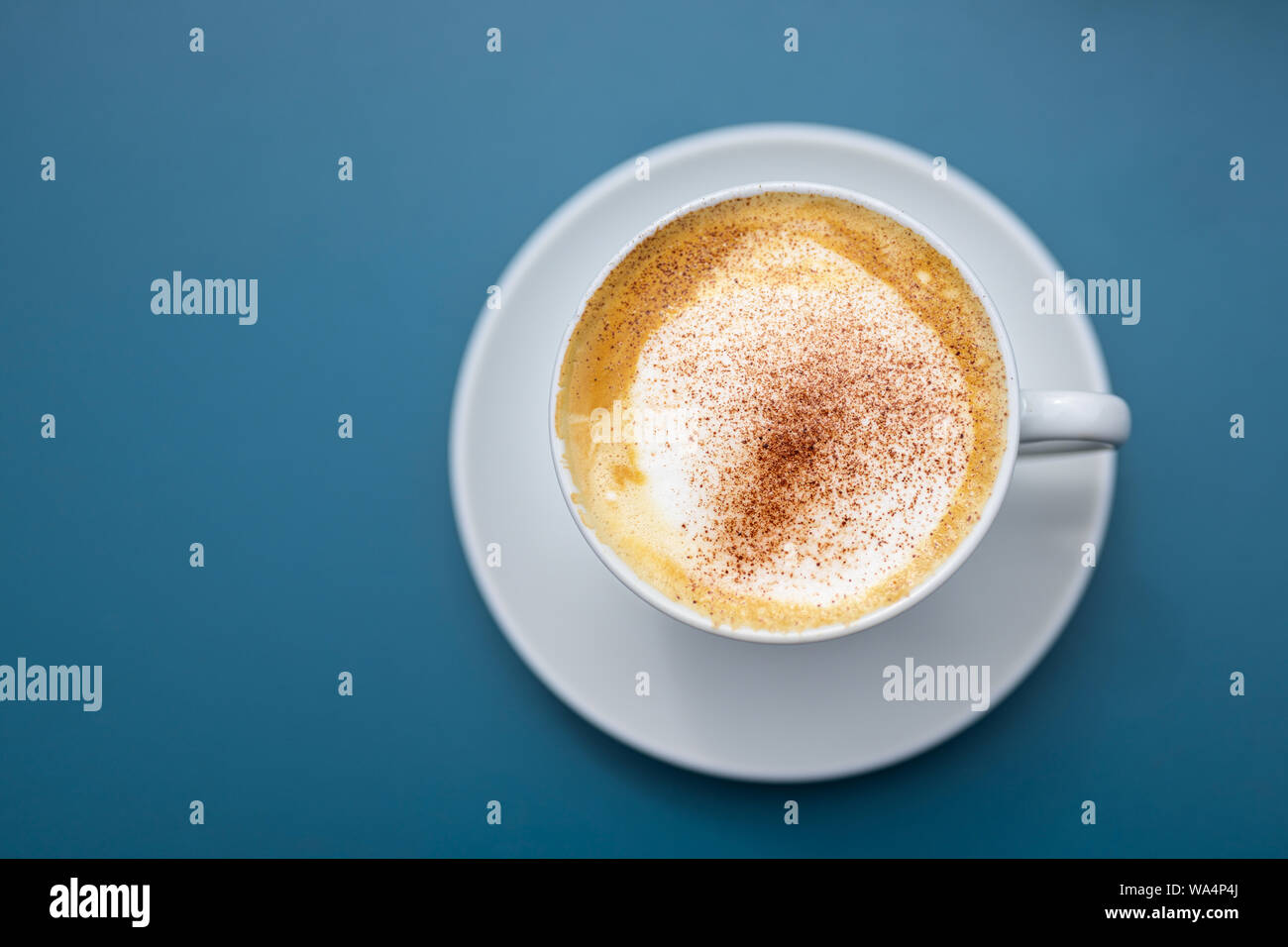 Tasse Cappuccino mit Kakaopulver auf einem blauen Hintergrund, direkt von oben ansehen, kopieren, ausgewählte konzentrieren, sehr enge Tiefenschärfe Stockfoto