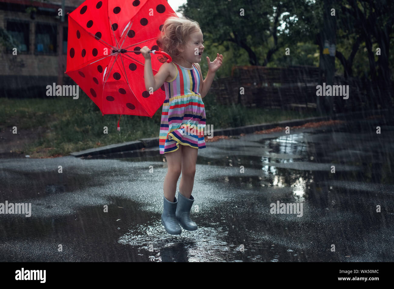 Süße Mädchen Kind mit Regenschirm springt im Regen durch die Pfützen. Stockfoto