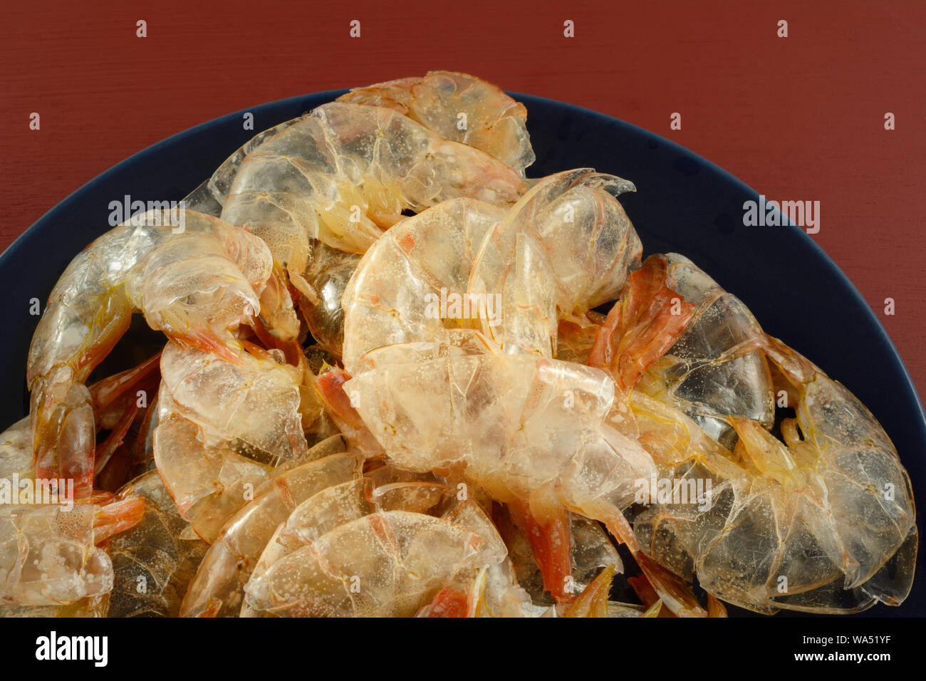 Vorbereitung oder Essen Mahlzeit mit leeren Garnelen Muscheln auf blauen Platte gestapelt auf dem roten Tisch Stockfoto