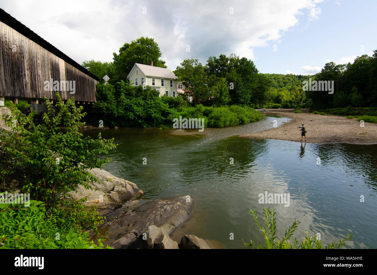 Mit einer überdachten Brücke vor ihm, eine Fliege Fischer wirft seine Linie auf die Mad River in Waitsfield, Vermont. Stockfoto