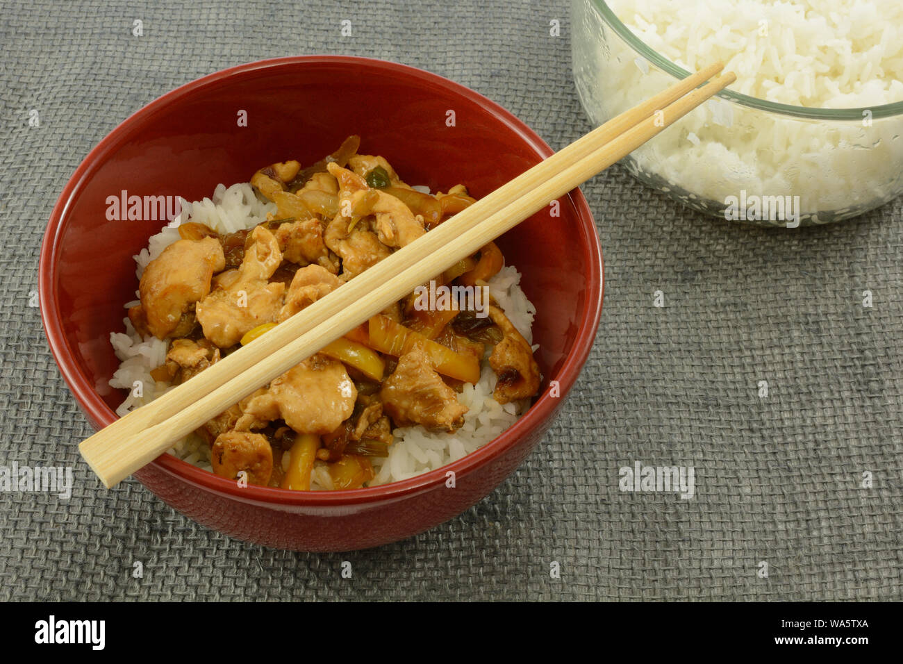 Rot Schüssel mit der Chicken Teriyaki auf weißem Reis mit Essstäbchen aus Holz und warme Schüssel mit gedämpftem Reis Stockfoto