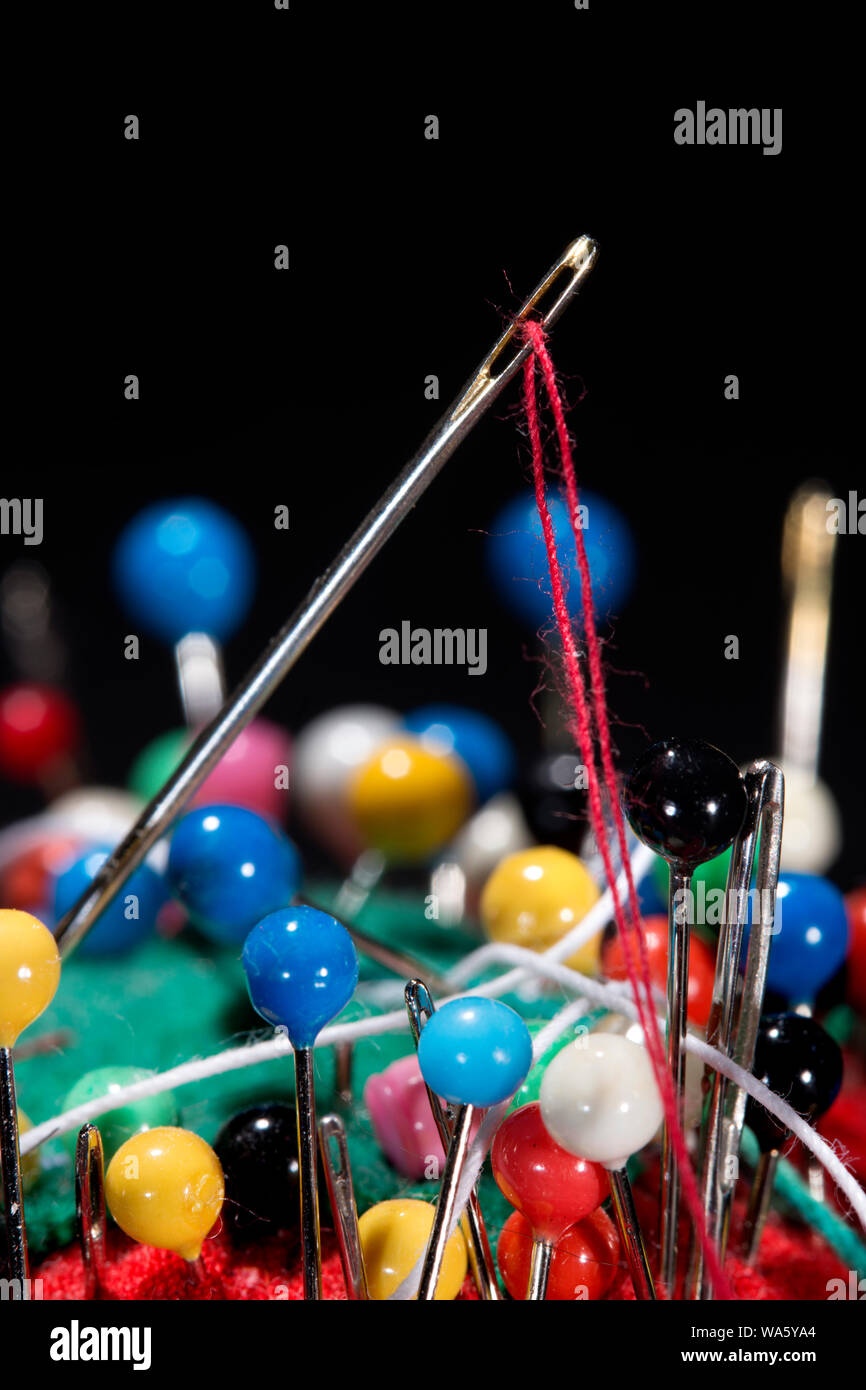 Nahaufnahme von nähen Werkzeuge. Nadel und roter Faden klemmt in Stift Kissen mit vielen bunten stick Pins, alle auf schwarzem Hintergrund; Stockfoto