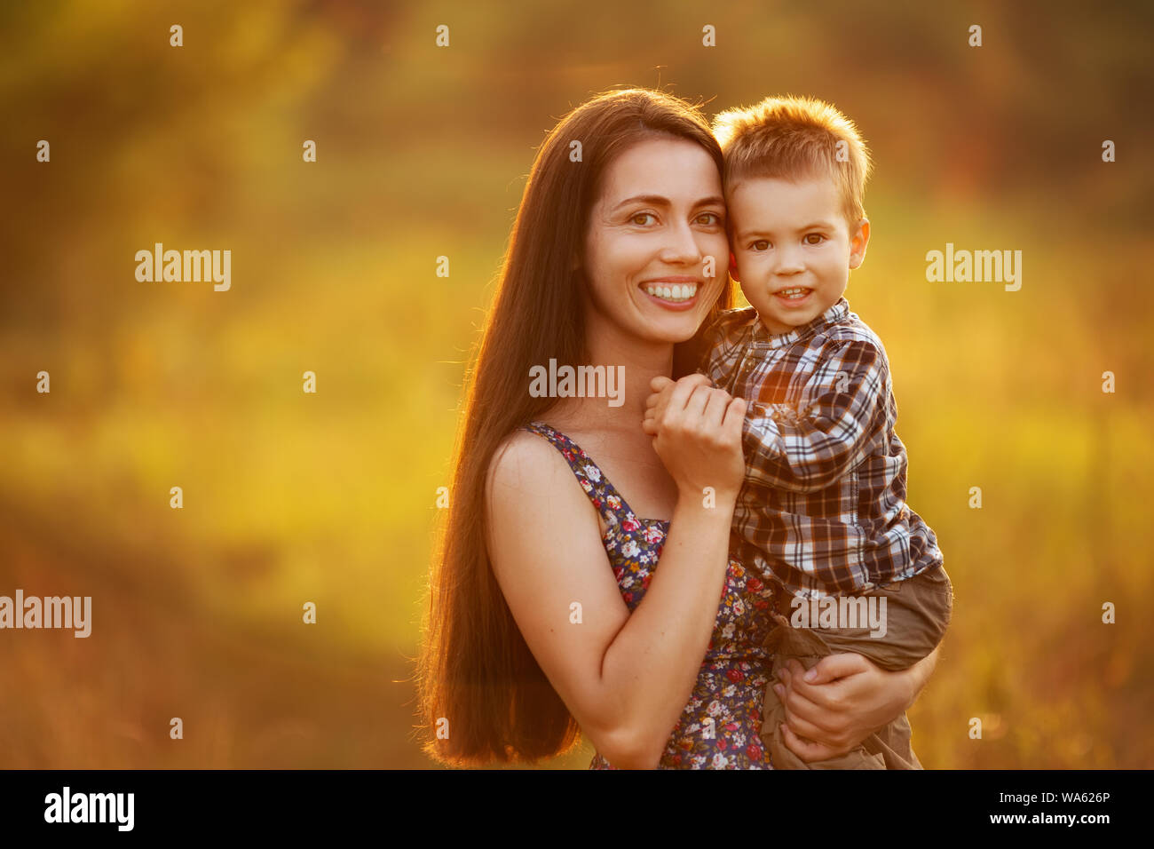 Glückliche Mutter mit Kleinkind Junge auf der Wiese am Sonnenuntergang. Schöne Frau, ihren Sohn im Freien halten. Familie Wandern im Sommer Natur Stockfoto