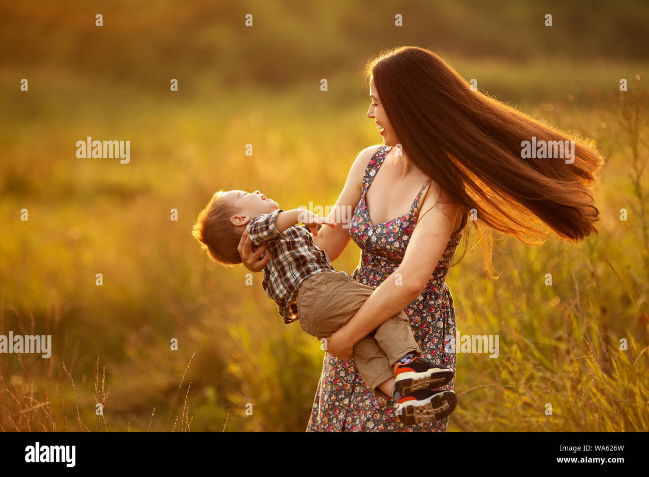 Glückliche Mutter mit Kleinkind Junge spielt auf der Wiese am Sonnenuntergang. Schöne Frau Spinnen ihr Sohn im Freien. Familie Wandern im Sommer Natur Stockfoto