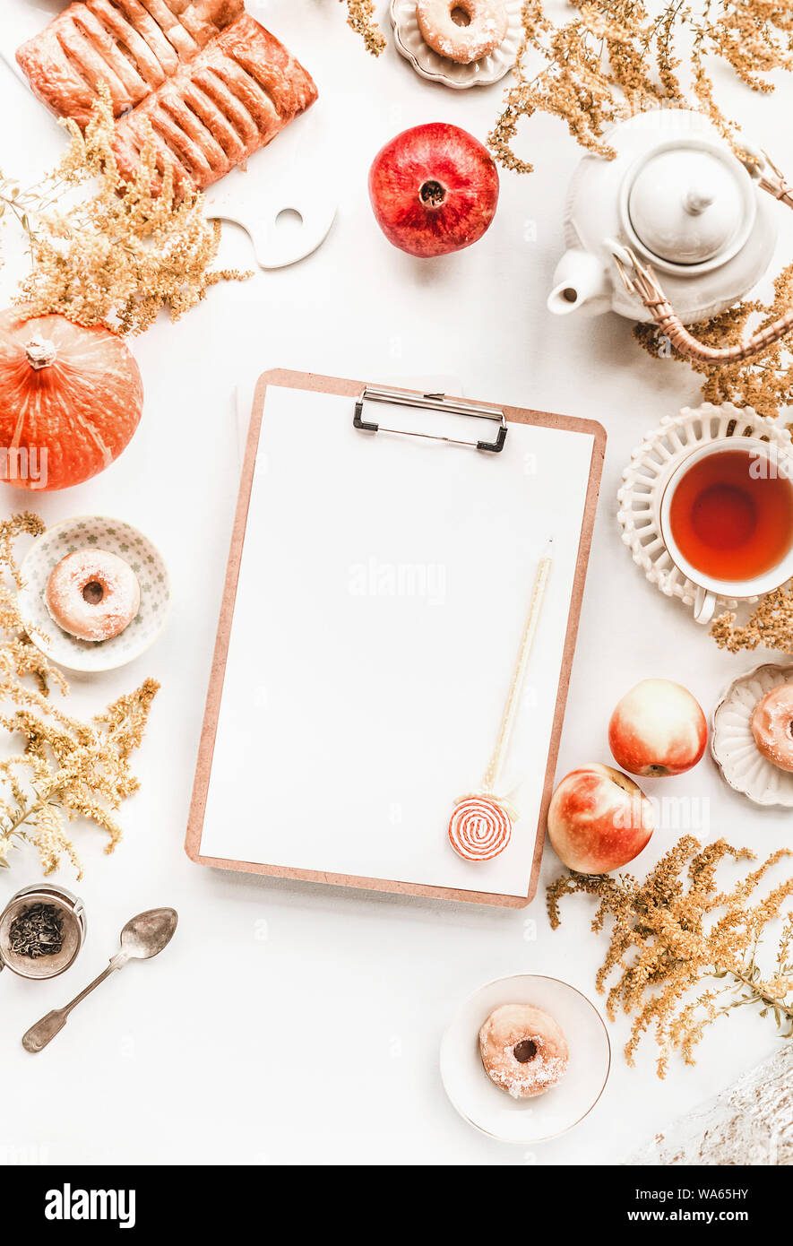 Schöne Herbst flach mit leeren Zwischenablage und Stift auf weißem Desktop mit Kürbis, Granatapfel, Äpfel, Kaffee, Donuts, Gebäck und Blumen. Top vie Stockfoto