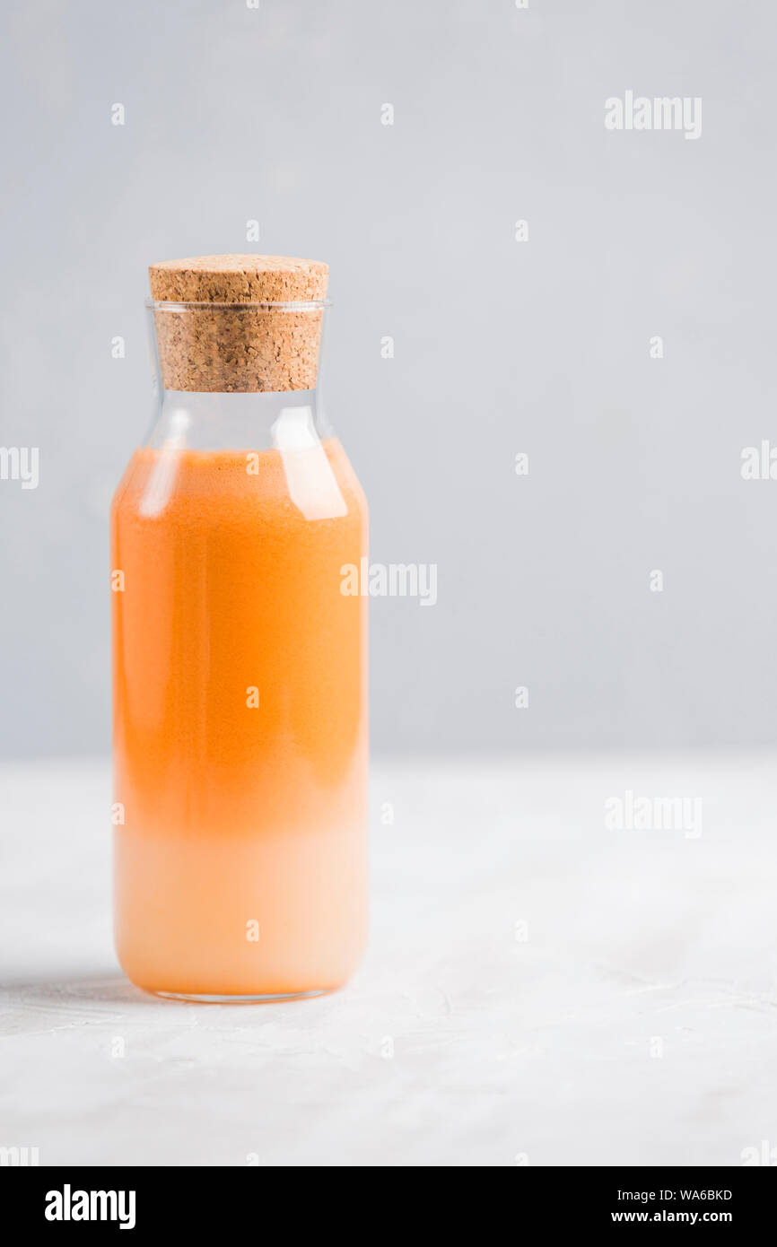 Frische Karotten Saft mit hafermilch und Minze. Vegetarische Getränk für gesundes Essen in eine durchsichtige Flasche mit einem hölzernen Anschlag auf einem hellen Hintergrund nach oben v Stockfoto