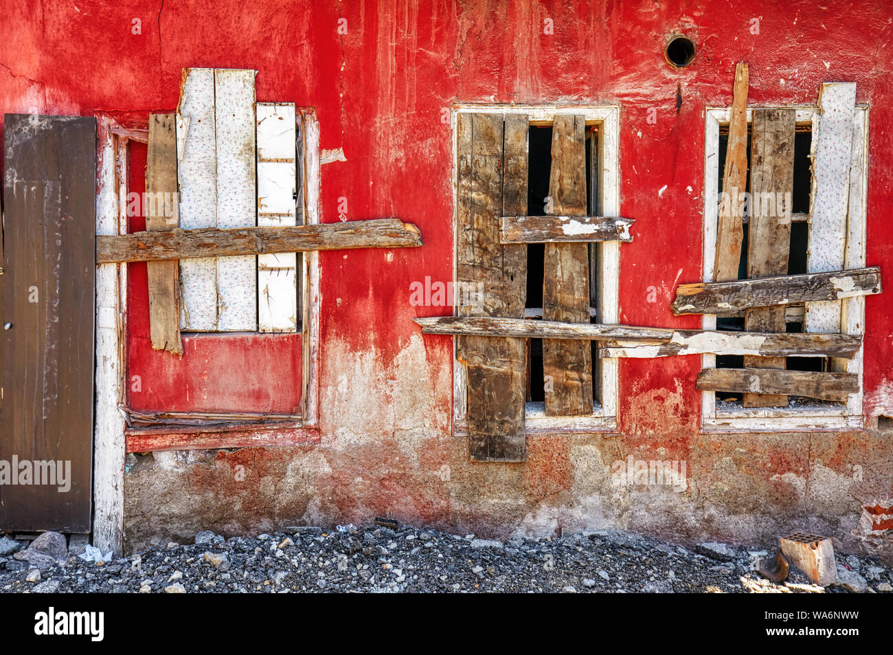 Nahaufnahme der Außenansicht eines verlassenen shanty Haus mit roten Wand und drei Fenster gesperrt mit Holzbohlen herunterfahren Stockfoto