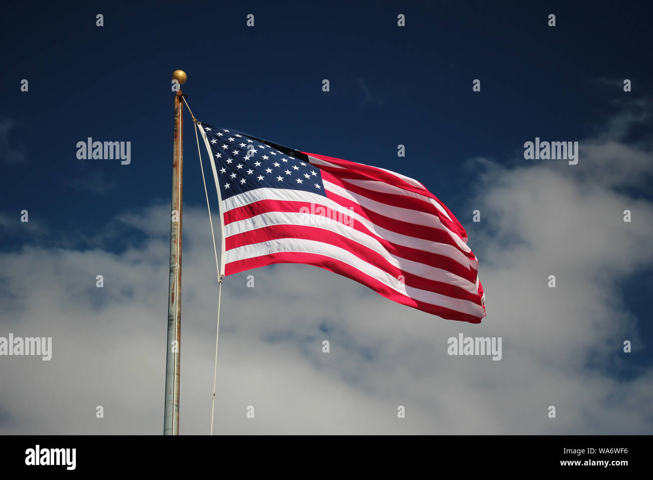 Amerikanische Flagge auf einer Stange schwankend gegen eine lebendige blauer Himmel mit weißen Wolken Stockfoto