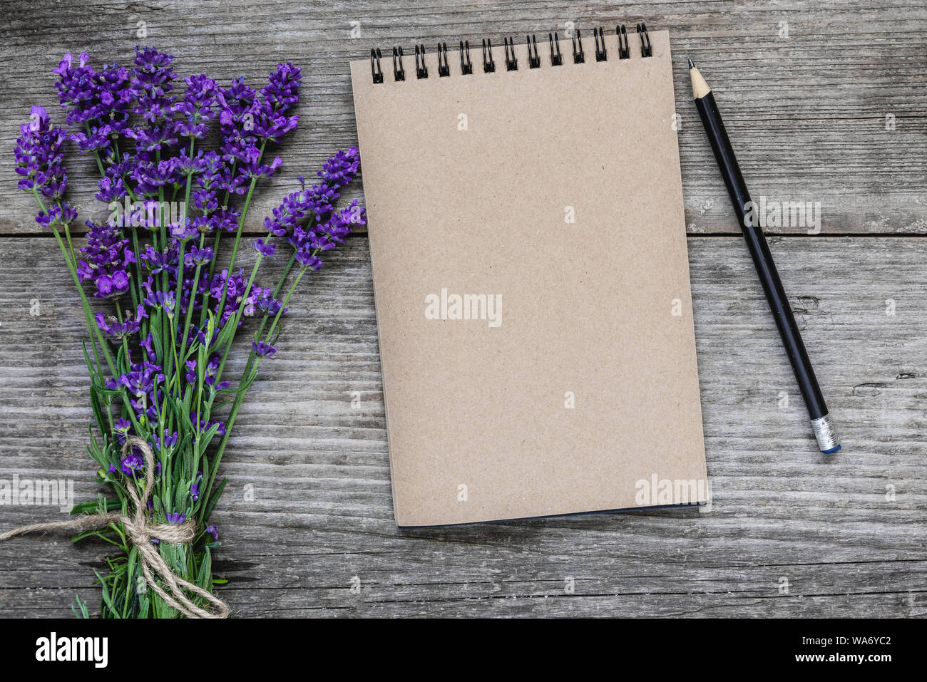 Lavendelblüten mit leeren Notizbuch aus Papier und Bleistift auf rustikalen Holzmöbeln Hintergrund. Flach. Mock up. festliche Hintergrund. top View Stockfoto