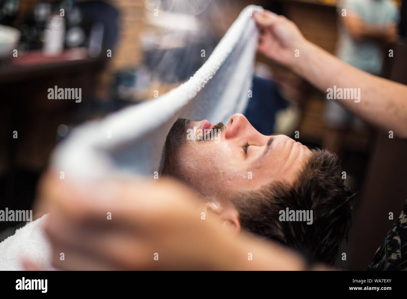 Friseur deckt das Gesicht eines Mannes mit einem warmen Handtuch. Traditionelle Ritual der Rasur des Bartes heiße und kalte Kompressen in einem alten Stil Friseur. Stockfoto