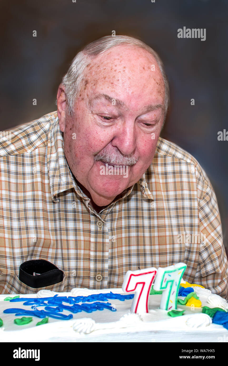 Ein älterer Mann bläst die Kerzen auf dem Kuchen für seinen 77. Geburtstag Stockfoto