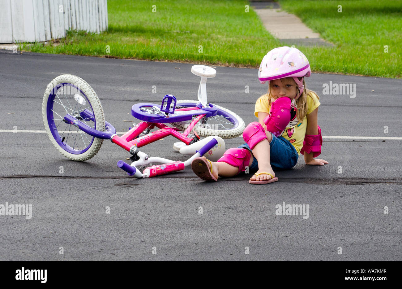 Ein kleines Mädchen in Sicherheitsausrüstung sitzt mitten in einer Fahrt, nachdem es von ihrem neuen Fahrrad gefallen ist. Stockfoto