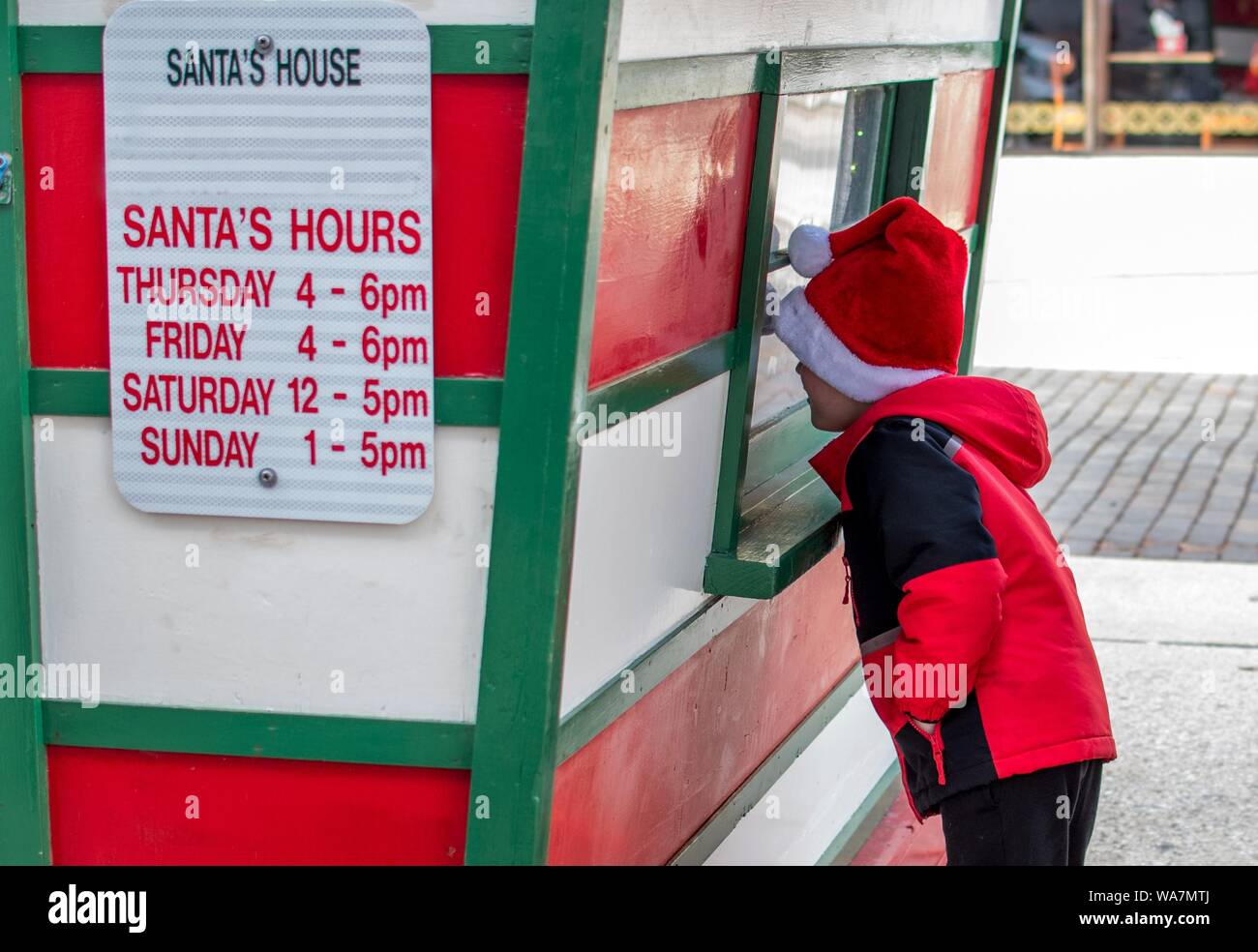 Kleiner Junge trägt eine Santa hat, sieht durch das Fenster, um zu sehen, ob Santa Es ist innen Stockfoto