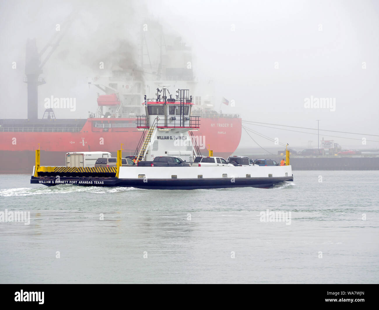 William G. Burnett Fähre Transporte Fahrzeuge über Corpus Christi Ship Channel im Nebel. Port Aransas, Texas USA. Tanker im Hintergrund. Stockfoto