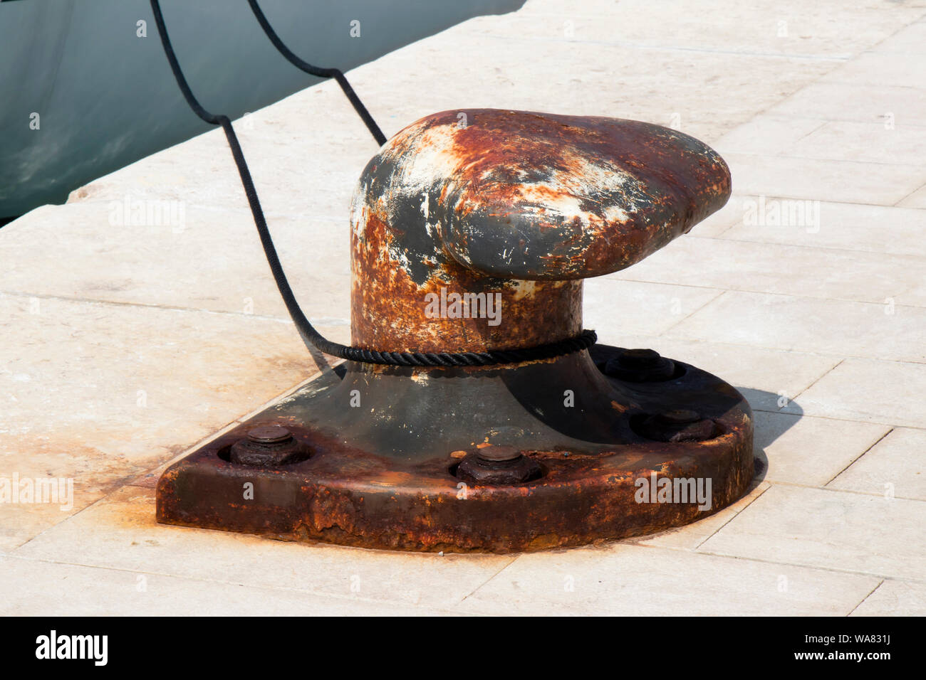 Große alte rostige Poller mit einem schwarzen Seil auf einem steinernen Pier Stockfoto