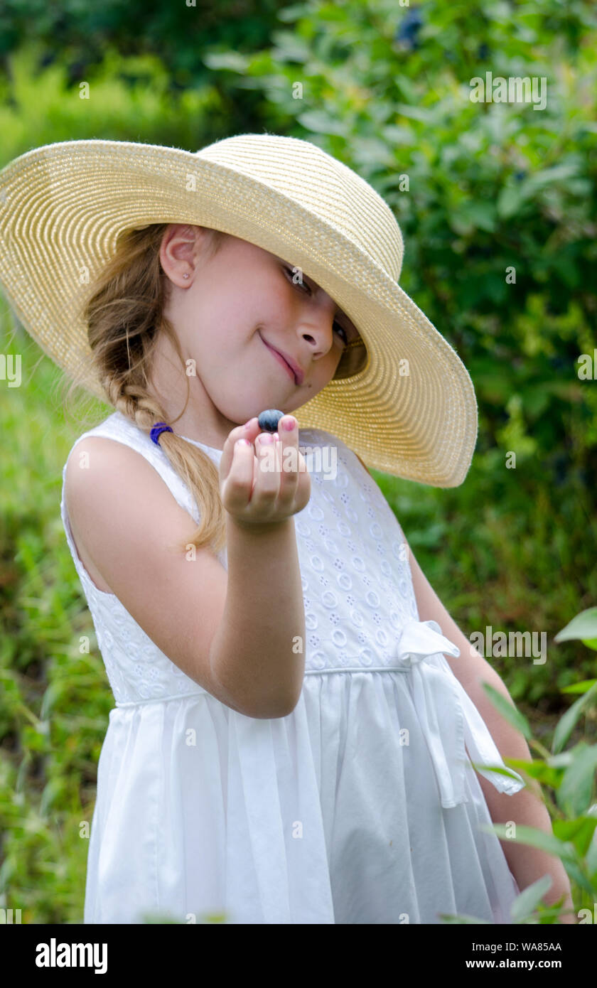 Eine liebenswerte Kind in einer Diskette Strohhut ist heraus halten, frische Blaubeeren zu Probe Stockfoto